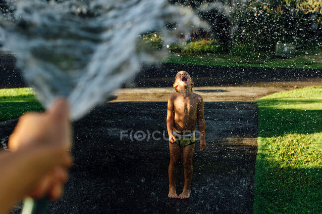 Chico disfrutando de salpicaduras de agua bajo el sol - foto de stock