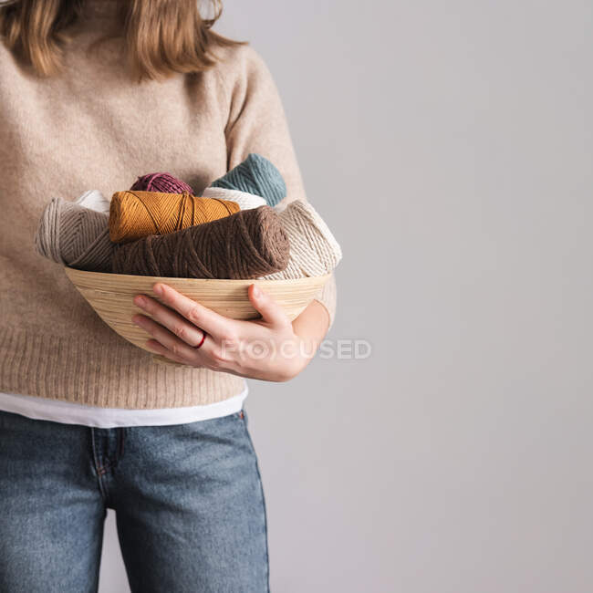 Knitting threads held in  woman's hands. Female person posing with a bowl full of ropes against the neutral grey background. Concept of handcraft hobby — Stock Photo