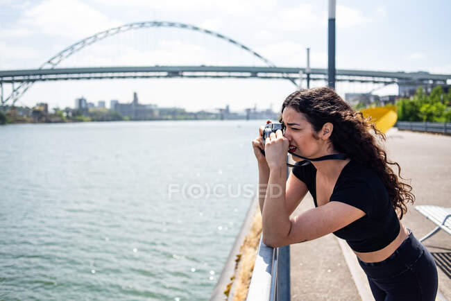 Молодая женщина фотографирует камеру на берегу реки — стоковое фото