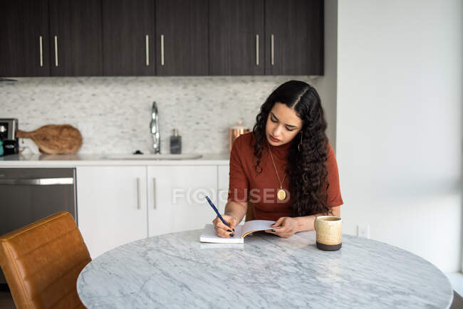 Mujer joven leyendo libro en la cocina - foto de stock