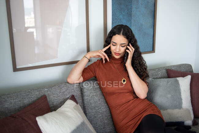 Молода жінка сидить на дивані і розмовляє по телефону — стокове фото