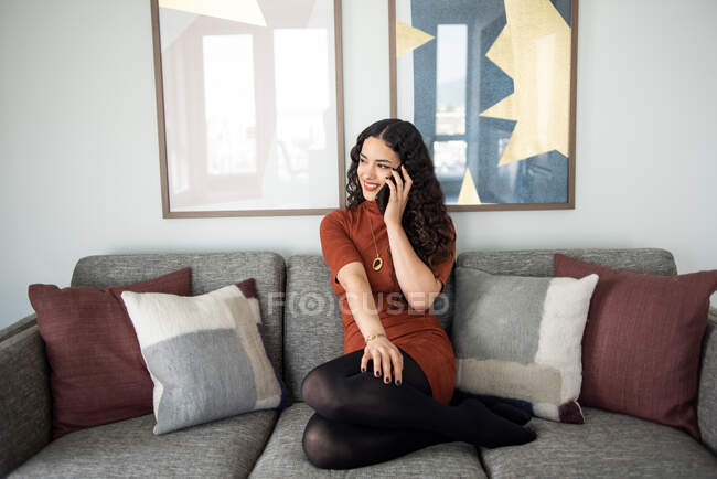 Молода красива жінка з кучерявим волоссям сидить на дивані і дивиться на камеру — стокове фото