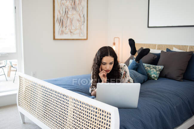 Красива молода жінка лежить на дивані і використовує ноутбук вдома . — стокове фото