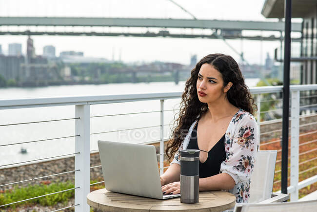 Mujer joven sentada en una mesa con portátil y taza de café - foto de stock