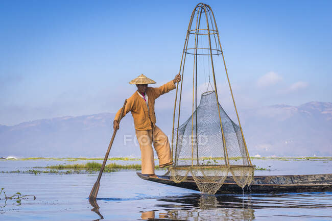 Intha fisherman with traditional conical fishing net against cle — Stock Photo
