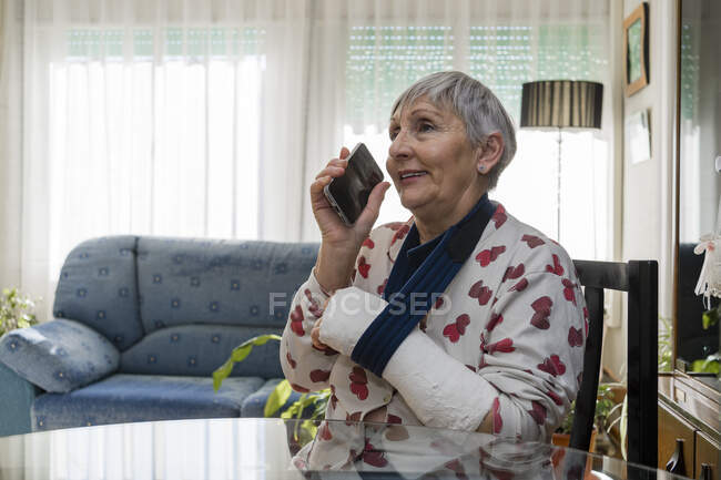 Caucasian white-haired elderly woman with broken arm, sitting at home — Stock Photo