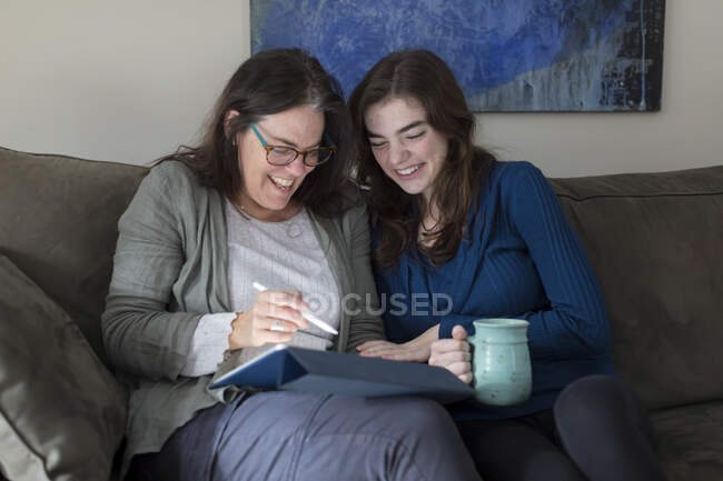A mother and daughter laugh while looking at a tablet together — Stock Photo