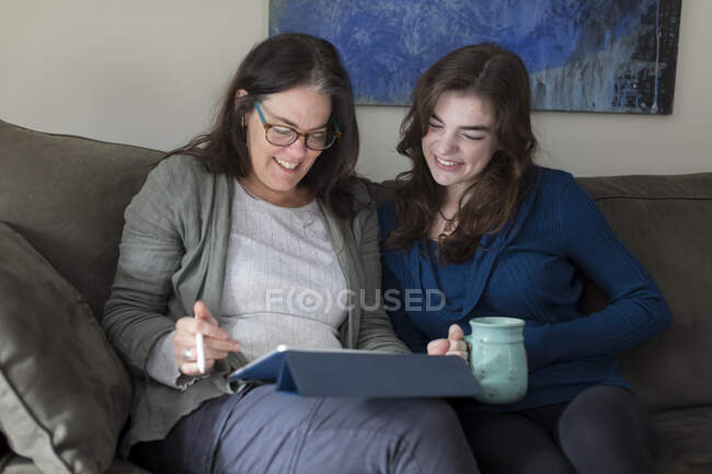Una madre y una hija sonríen mientras miran una tableta juntas - foto de stock