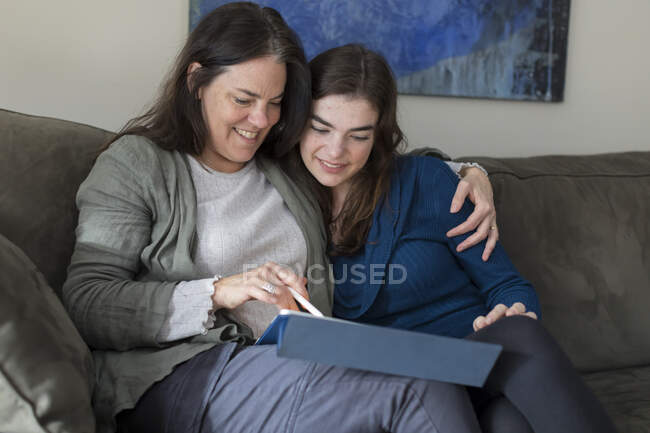 Madre con el brazo alrededor hija adolescente sonriendo y mirando a la tableta - foto de stock