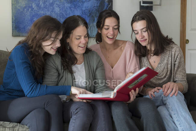 Мати і три дочки сміються, дивлячись на фотоальбом — стокове фото