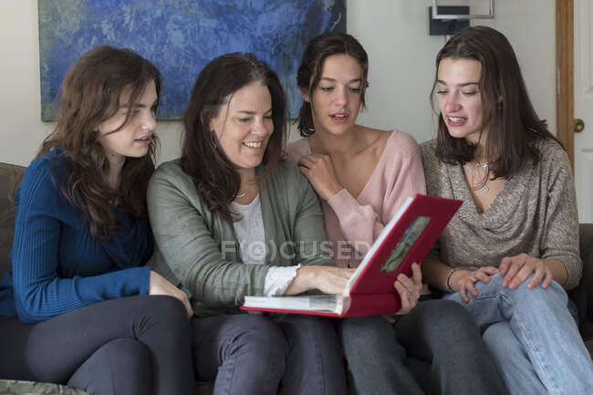 Una madre y sus tres hijas miran juntos un álbum de fotos - foto de stock