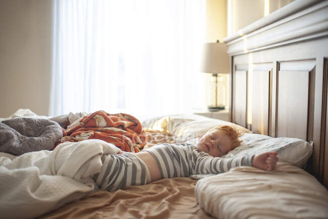 Bambino ragazzo 3-4 anni addormentato in disordinato genitori letto in bella luce — Foto stock