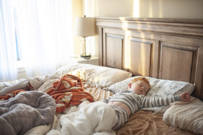 Enfant garçon 3-4 ans endormi dans un lit de parents désordonné dans une jolie lumière — Photo de stock