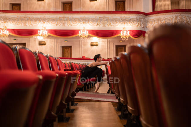Ballerina appoggiata sul sedile e in attesa di spettacolo mentre seduto vicino alla navata in teatro — Foto stock
