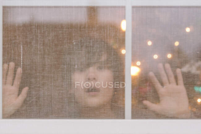 A young boy presses his face and hands up to a screened window — Stock Photo
