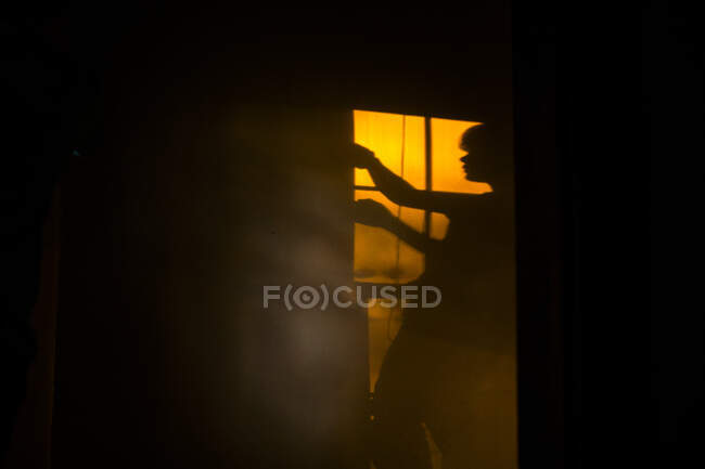 Schatten eines Kindes, das bei Sonnenuntergang an einem Fenster im goldenen Licht steht — Stockfoto