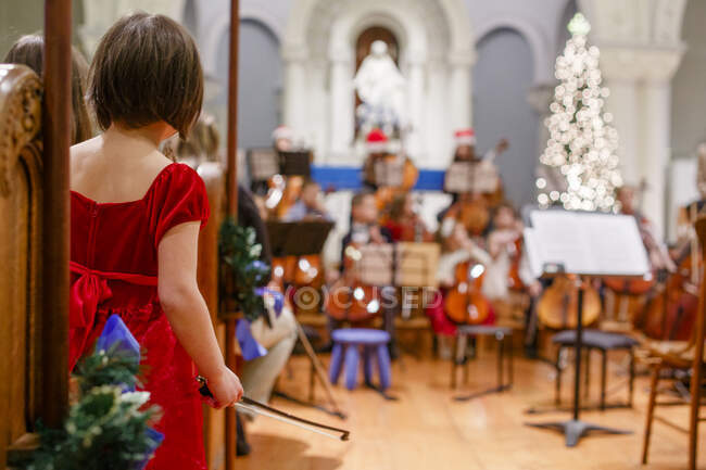 Una niña pequeña se para con el arco de violonchelo en la mano esperando su turno para realizar - foto de stock