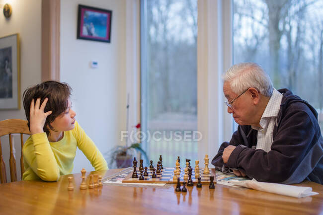 Um avô estuda cuidadosamente um tabuleiro de xadrez enquanto o neto olha — Fotografia de Stock