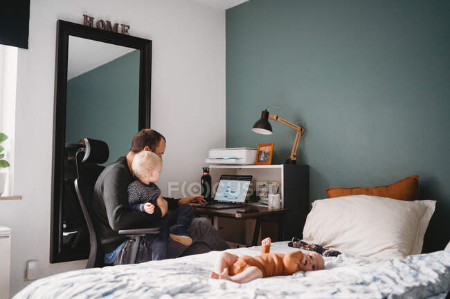 Pai com criança no colo fazendo escritório em casa durante a quarentena vívida — Fotografia de Stock