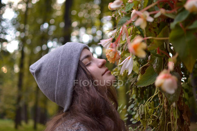 Uma menina de chapéu caminha no parque, apreciando o cheiro de flores. — Fotografia de Stock