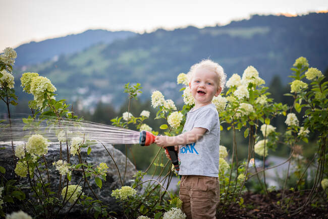 Un garçon riant et arrosant des fleurs — Photo de stock