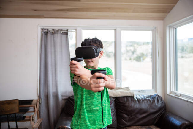Niño adolescente jugando con auriculares de realidad virtual en la sala de estar - foto de stock