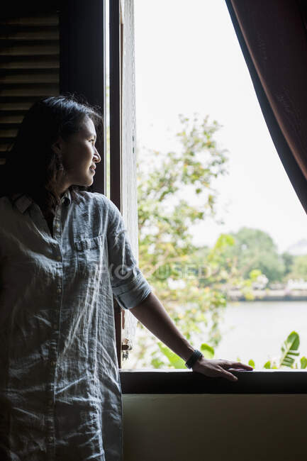 Belle femme regardant par la fenêtre à Bangkok — Photo de stock