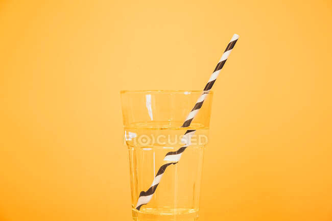 Bere paglia in un bicchiere d'acqua, luminoso sfondo giallo arancio studio. Idratante, acqua potabile, immagine vibrante del prodotto generico — Foto stock