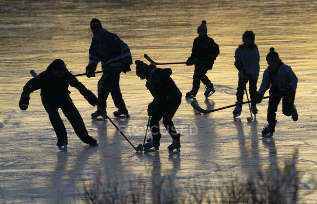 Hombres y niños jugando hockey estanque al atardecer - foto de stock