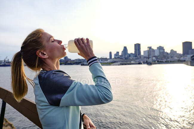 Mujer bebiendo agua con paisaje urbano detrás, Montreal, Quebec, Canadá - foto de stock