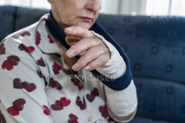 Caucasian senior woman with white hair with broken arm, sitting sofa — Stock Photo