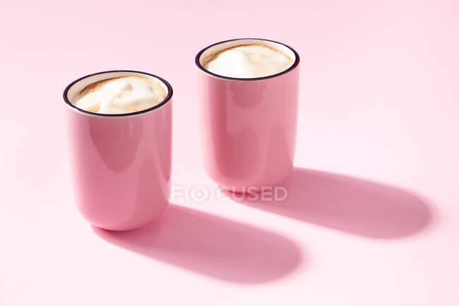 Deux tasses de cappuccino en tasses roses sur fond rose — Photo de stock