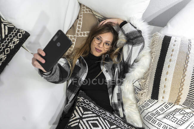 Молодая женщина отдыхает на диване, делая селфи со смартфоном — стоковое фото