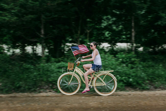 Ragazza in sella alla sua bici con una bandiera americana su una strada sterrata rurale — Foto stock