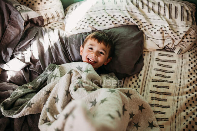 Mignon garçon souriant dans lit — Photo de stock