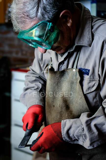 Man with gray hair and green goggles working in a workshop — Stock Photo