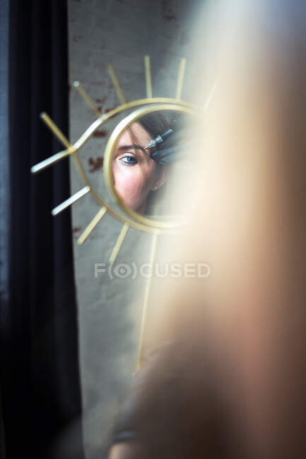 Eye in mirror of young beautiful woman hold permanent make up tool — Stock Photo
