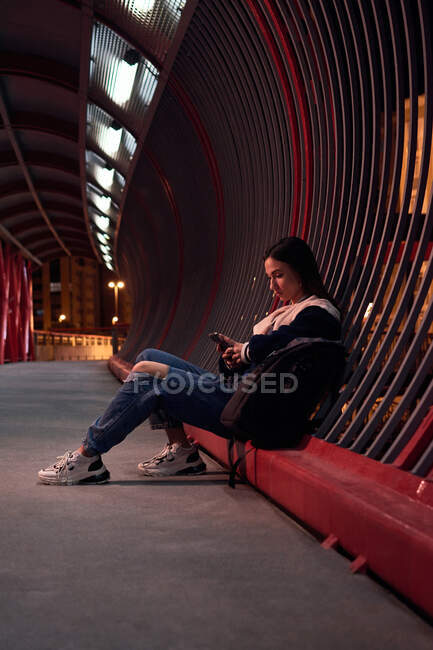 Jeune femme regarde son téléphone sur un pont rouge la nuit — Photo de stock