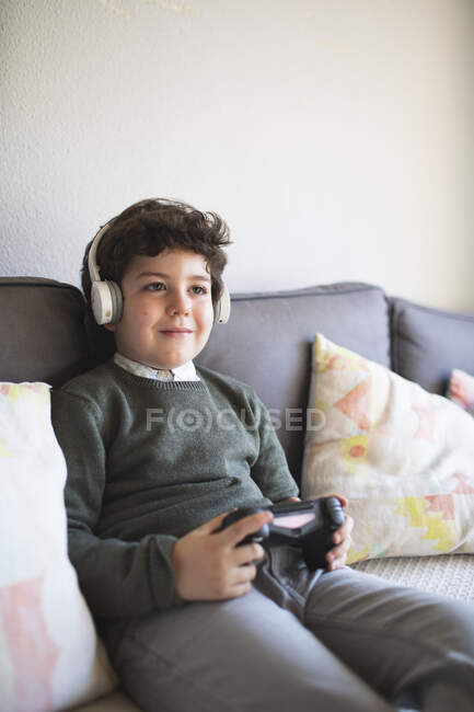 Bambino con un joystick sul viso mentre siede sul divano — Foto stock