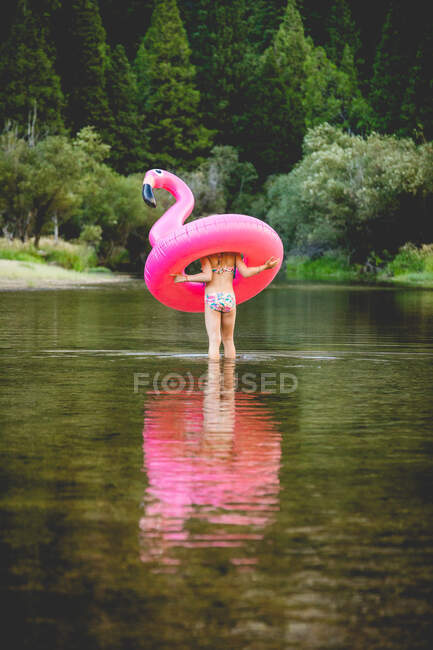 Menina percorrendo o rio e carregando flamingo flutuante — Fotografia de Stock