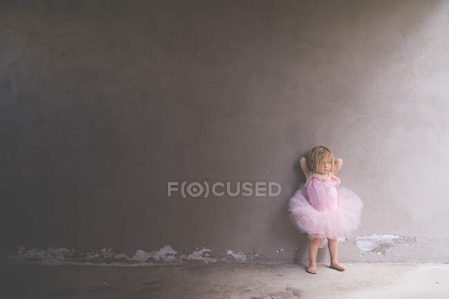 Little girl dressed in a too big ballerina outfit leaning against wall — Stock Photo