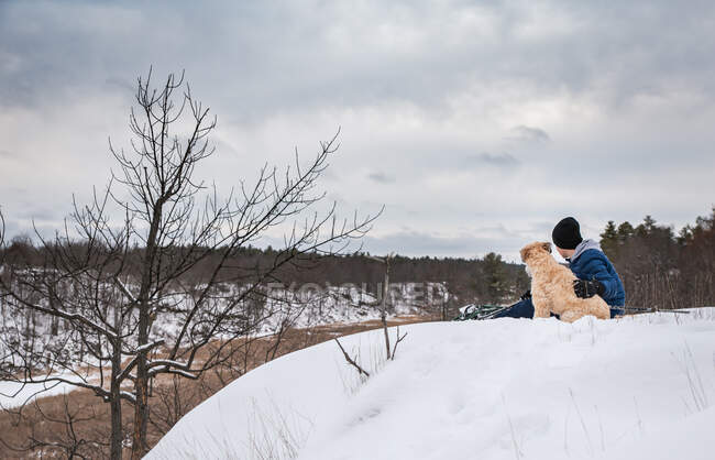 Young boy sitting with dog  in the snow — Stock Photo
