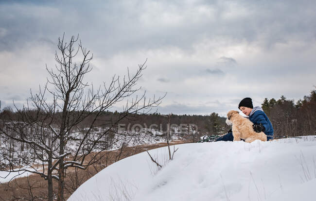 Jeune garçon assis avec chien dans la neige — Photo de stock