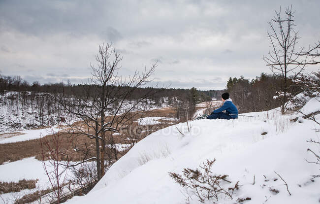 Мальчик, сидящий на снегу — стоковое фото