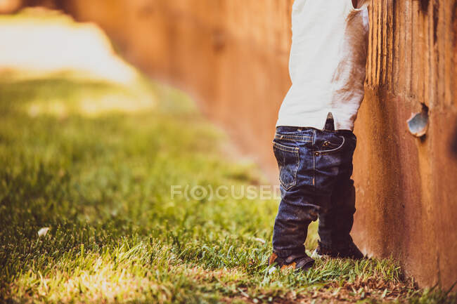 Bebé con jeans azules tratando de caminar cerca de una pared - foto de stock
