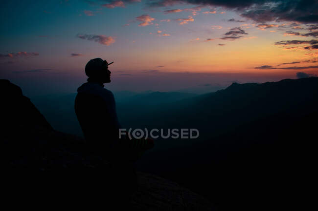 Un hombre mirando al atardecer en la cima de una montaña - foto de stock