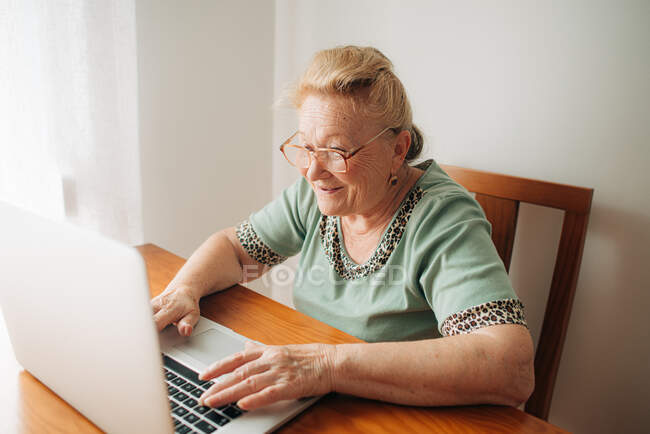 Старшая женщина улыбается, работая дома за компьютером — стоковое фото