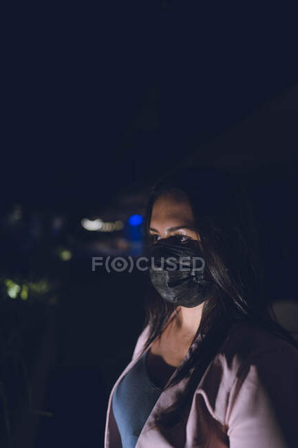 Frau trägt Gesichtsschutz schwarze Maske ihr Gesicht beleuchtet — Stockfoto