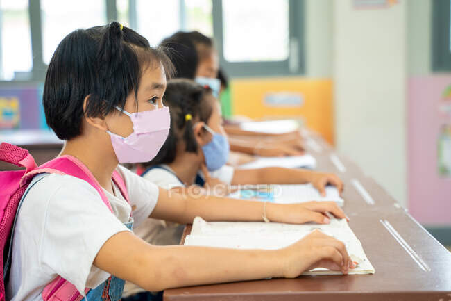 Шкільні діти носять захисні маски для обличчя для безпеки, сидячи в початковій школі, освіті, навчанні та концепції людей, Соціальна дистанція . — стокове фото