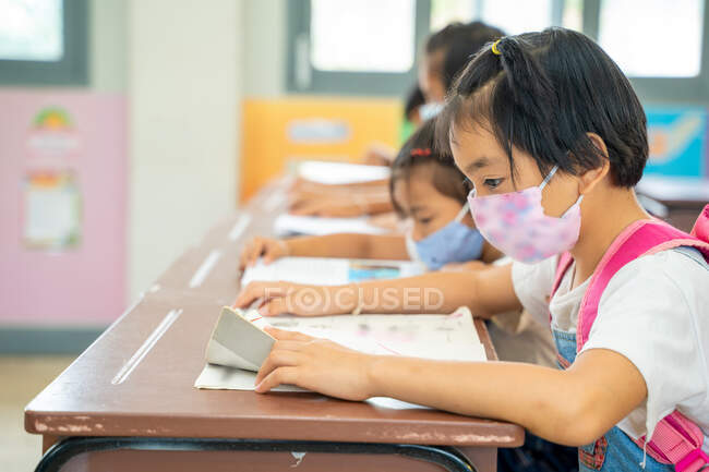 Grupo de crianças asiáticas usando máscara protetora para proteger contra Covid-19 sentado na mesa em sala de aula, Elementary school, Social Distancing, Coronavirus se transformou em uma emergência global. — Fotografia de Stock